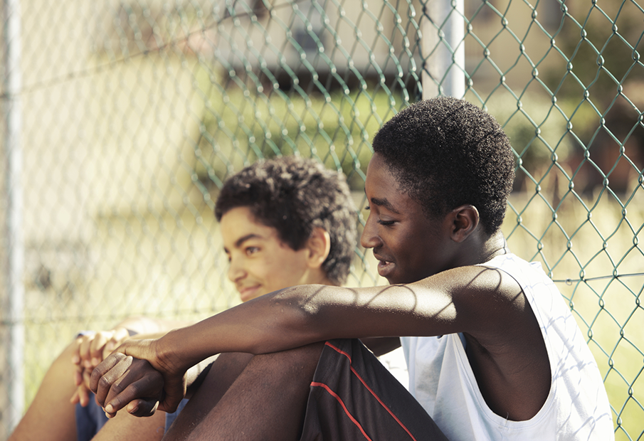 Two boys sitting outside a fence