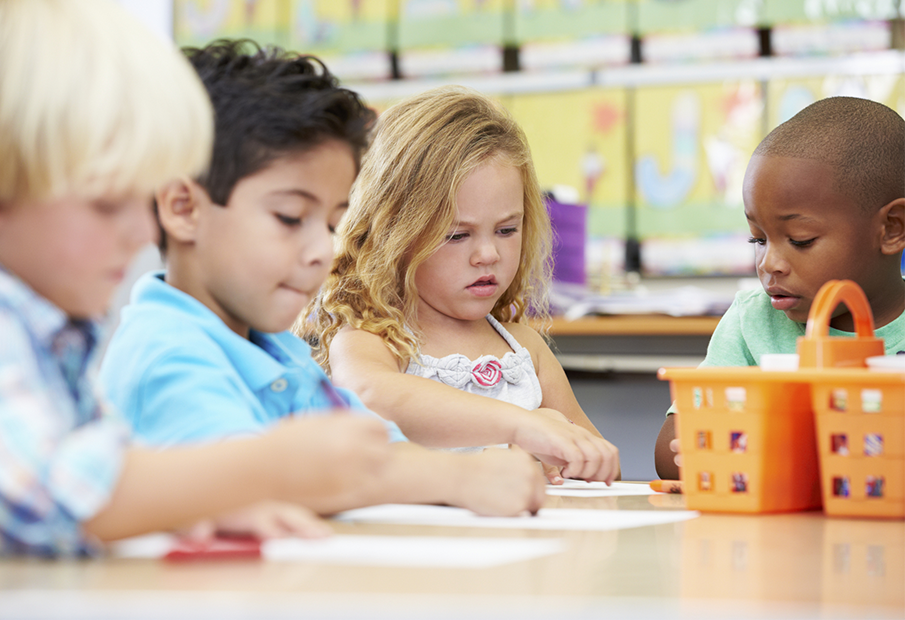 Four multicultural students in a classroom coloring