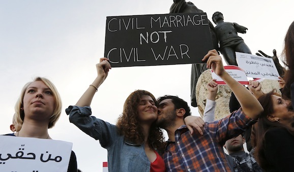 A man kisses a woman as they hold up a placard during a protest demanding to legalize civil marriage in Lebanon, at Martyrs' square in downtown Beirut February 4, 2013. Lebanese laws do not recognise civil marriages conducted in Lebanon. REUTERS/Jamal Saidi   (LEBANON - Tags: CIVIL UNREST) - RTR3DCHX