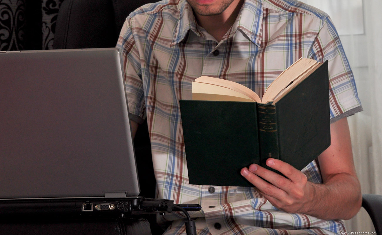 Student writing a paper from a book on a notebook computer
