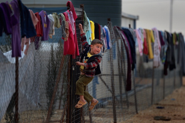 ZA'ATARI, JORDAN - FEBRUARY 01:  Young boy hangs on a fence with clothing hung from it, as Syrian refugees go about their daily business in the Za'atari refugee camp on February 1, 2013 in Za'atari, Jordan. Record numbers of refugees are fleeing the violence and bombings in Syria to cross the borders to safety in northern Jordan and overwhelming the Za'atari camp. The Jordanian government are appealing for help with the influx of refugees as they struggle to cope with the sheer numbers arriving in the country.  (Photo by Jeff J Mitchell/Getty Images)