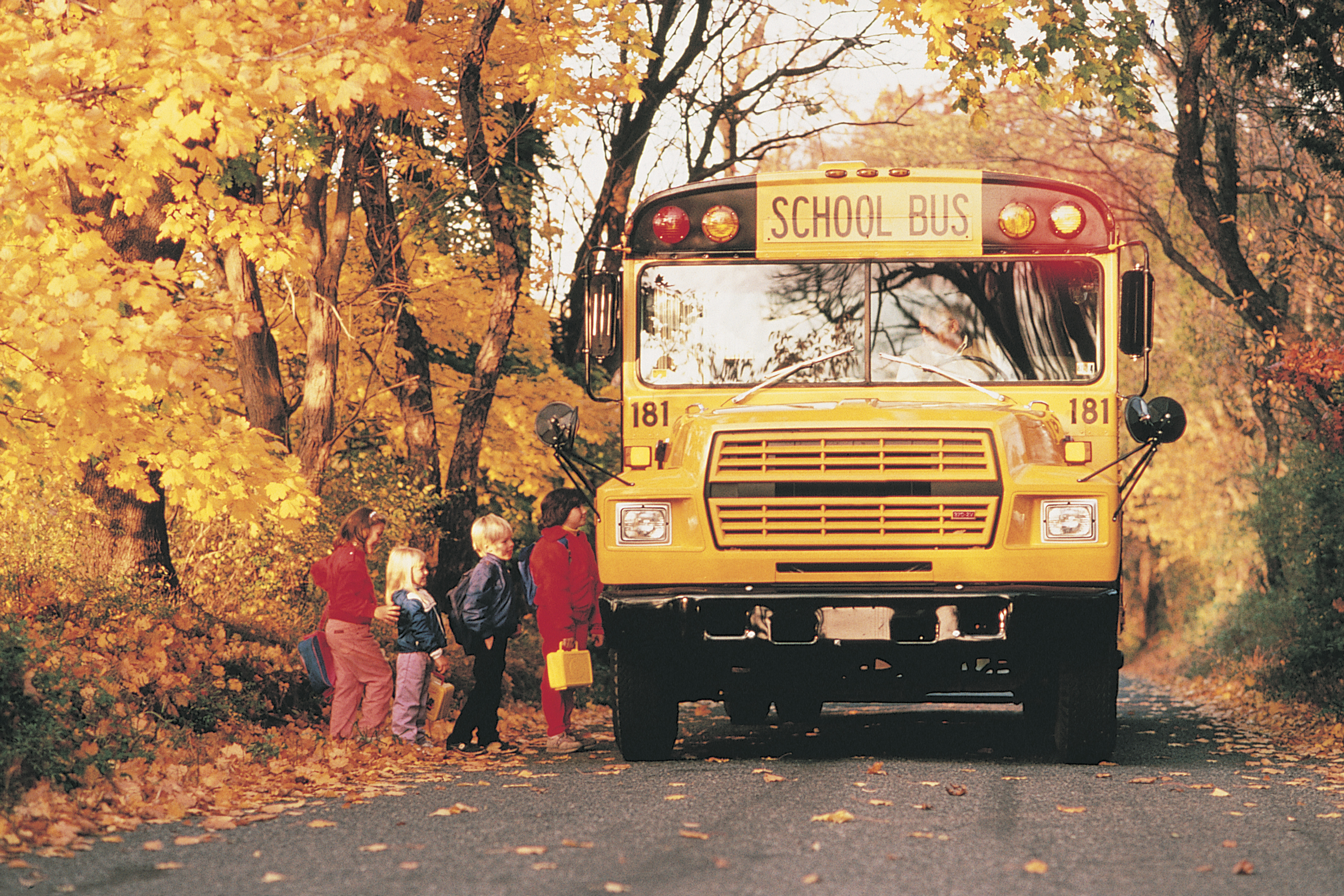 Children boarding school bus on rural road in autumn
