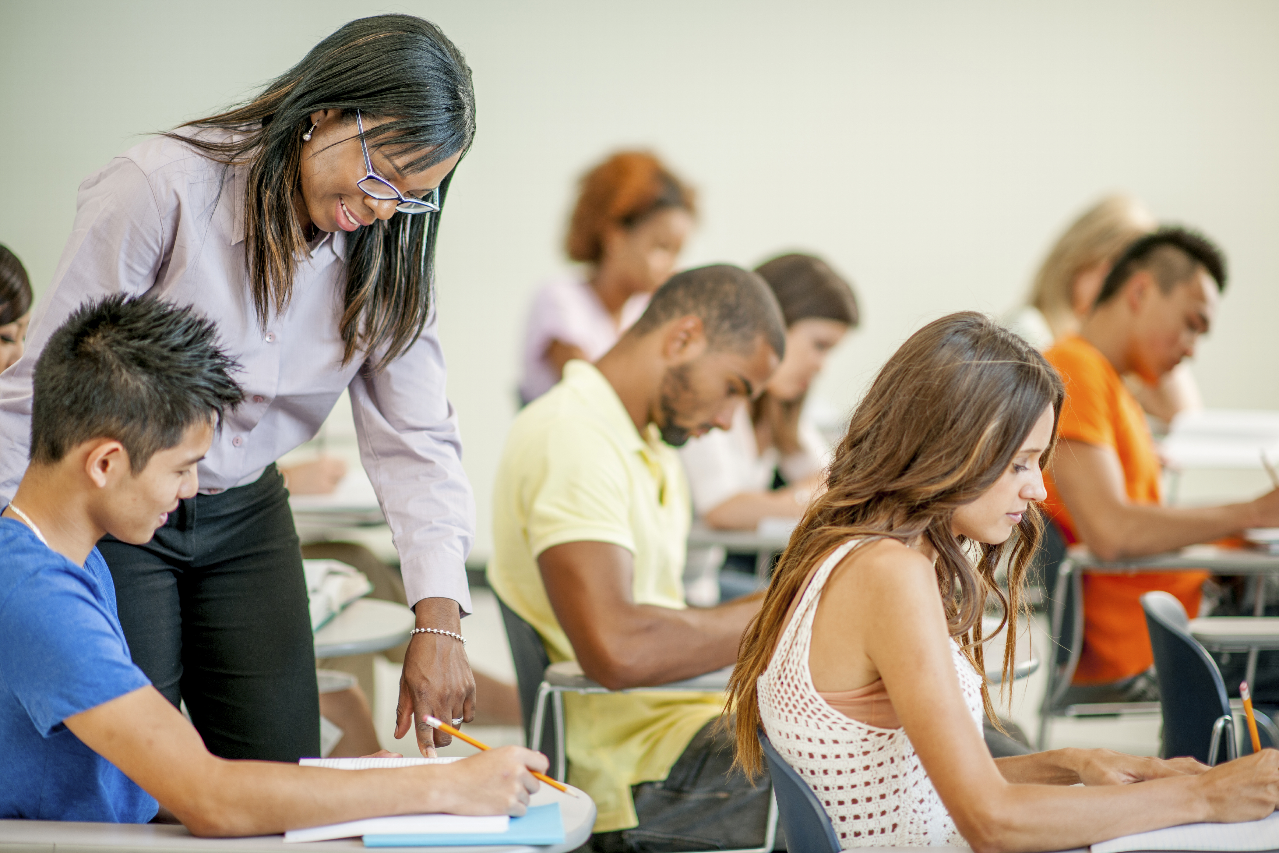 A multi-ethnic group of college age students are sitting in class and are working on an assignment.