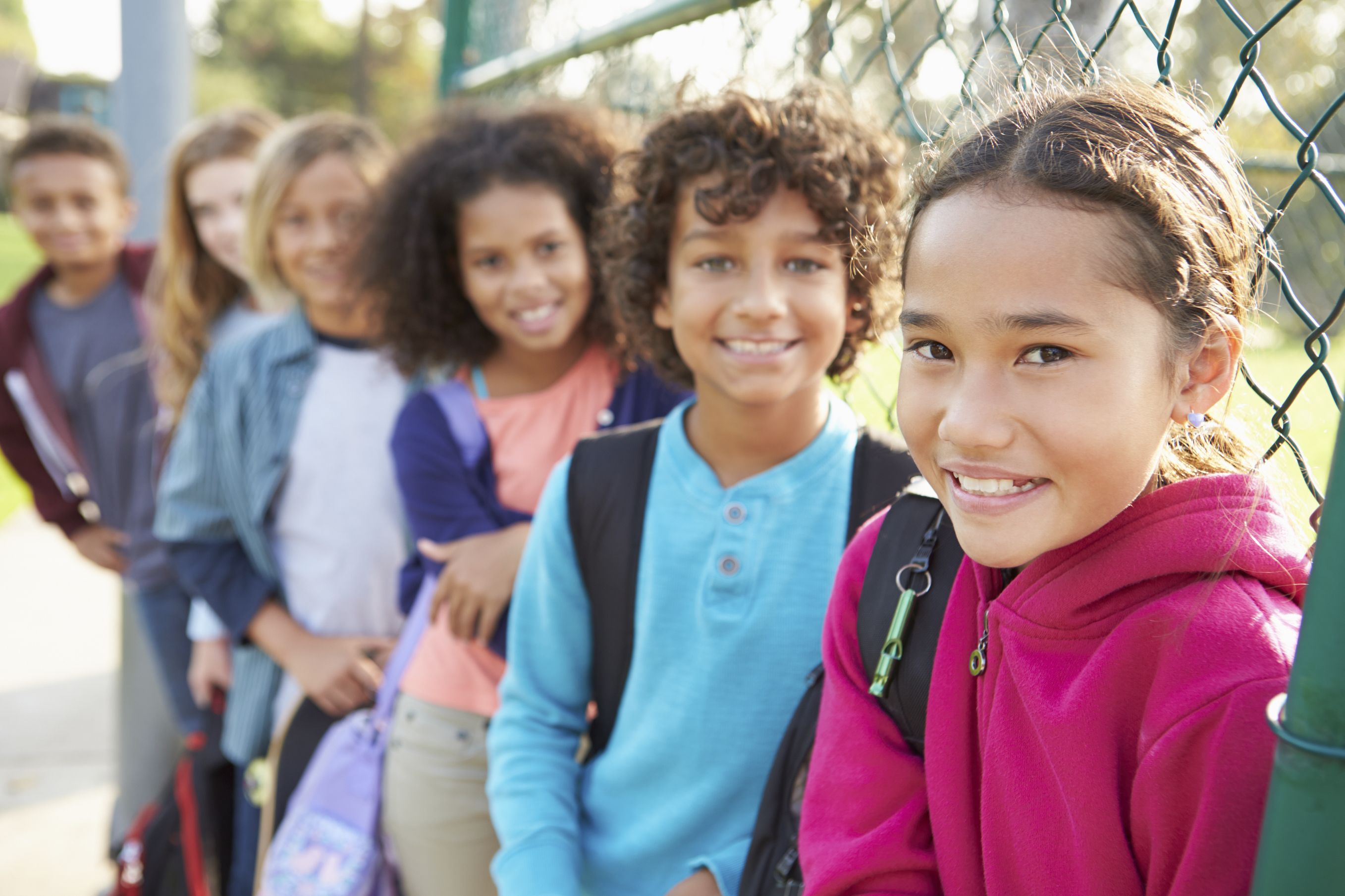 Group Of Young Children Hanging Out In Playground Smiling To Camera