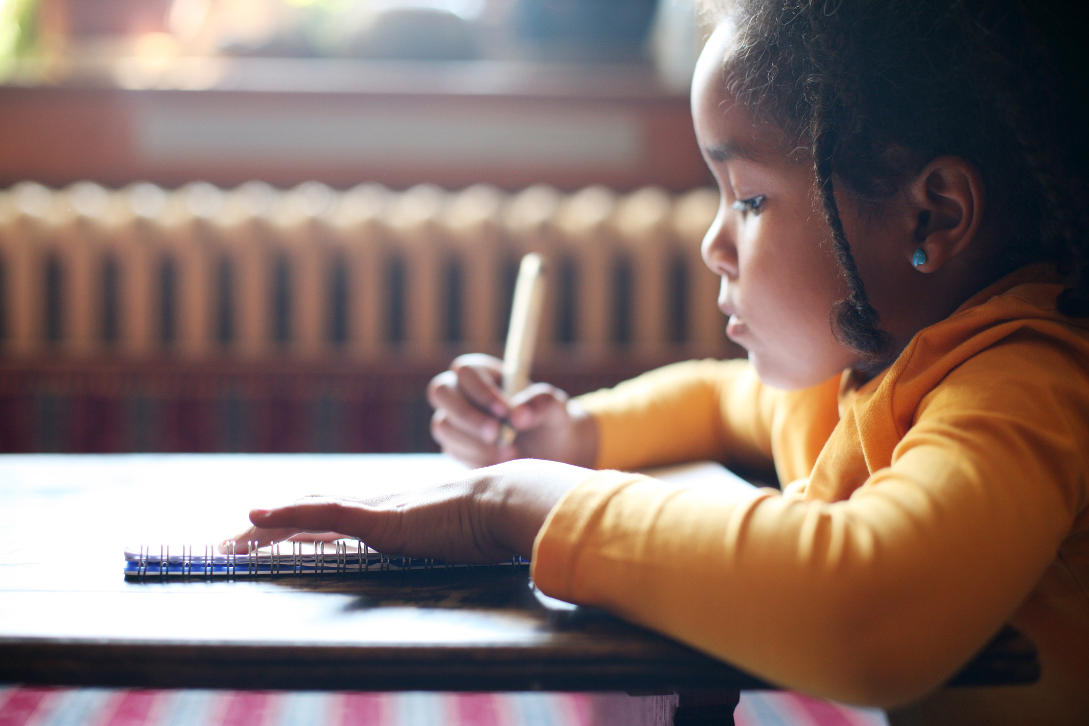 Profile of little African girl writing  in classroom.