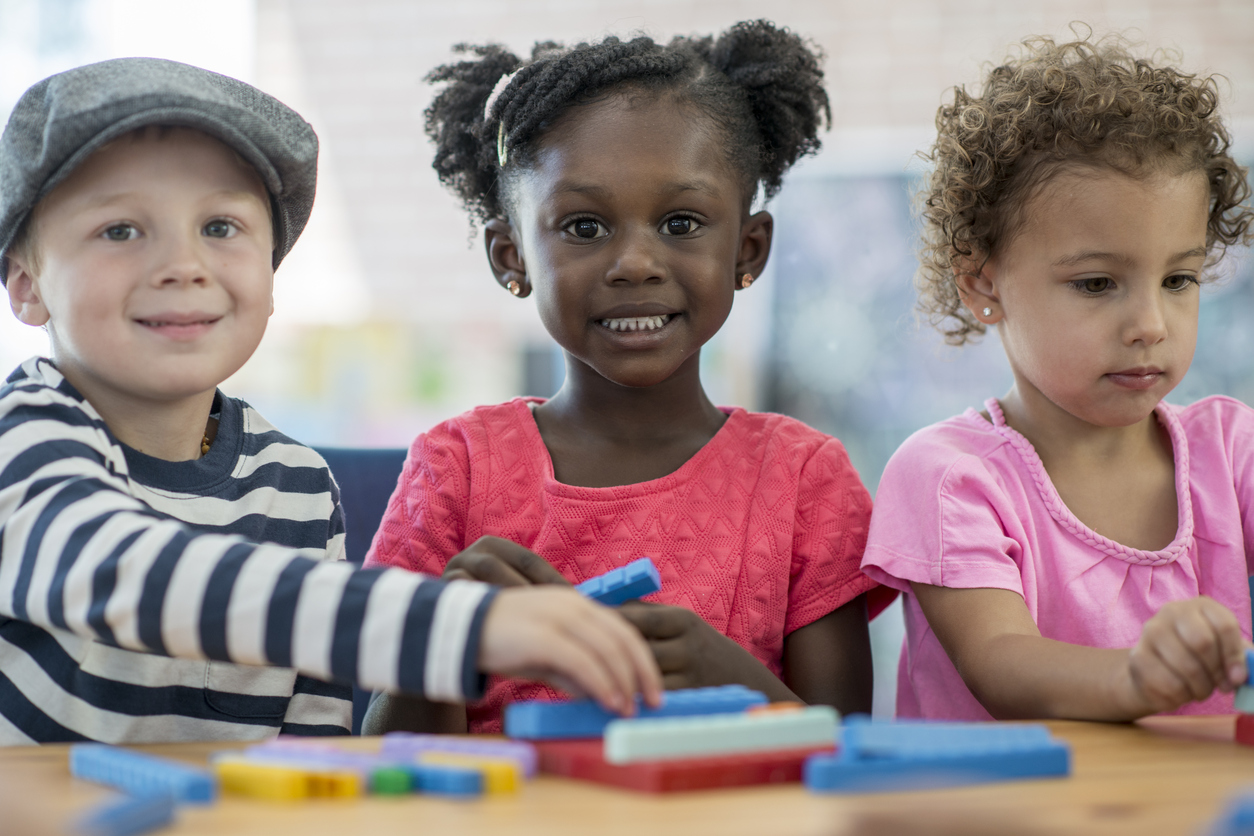 A multi-ethnic group of preschoolers are learning how to count with toys blocks.