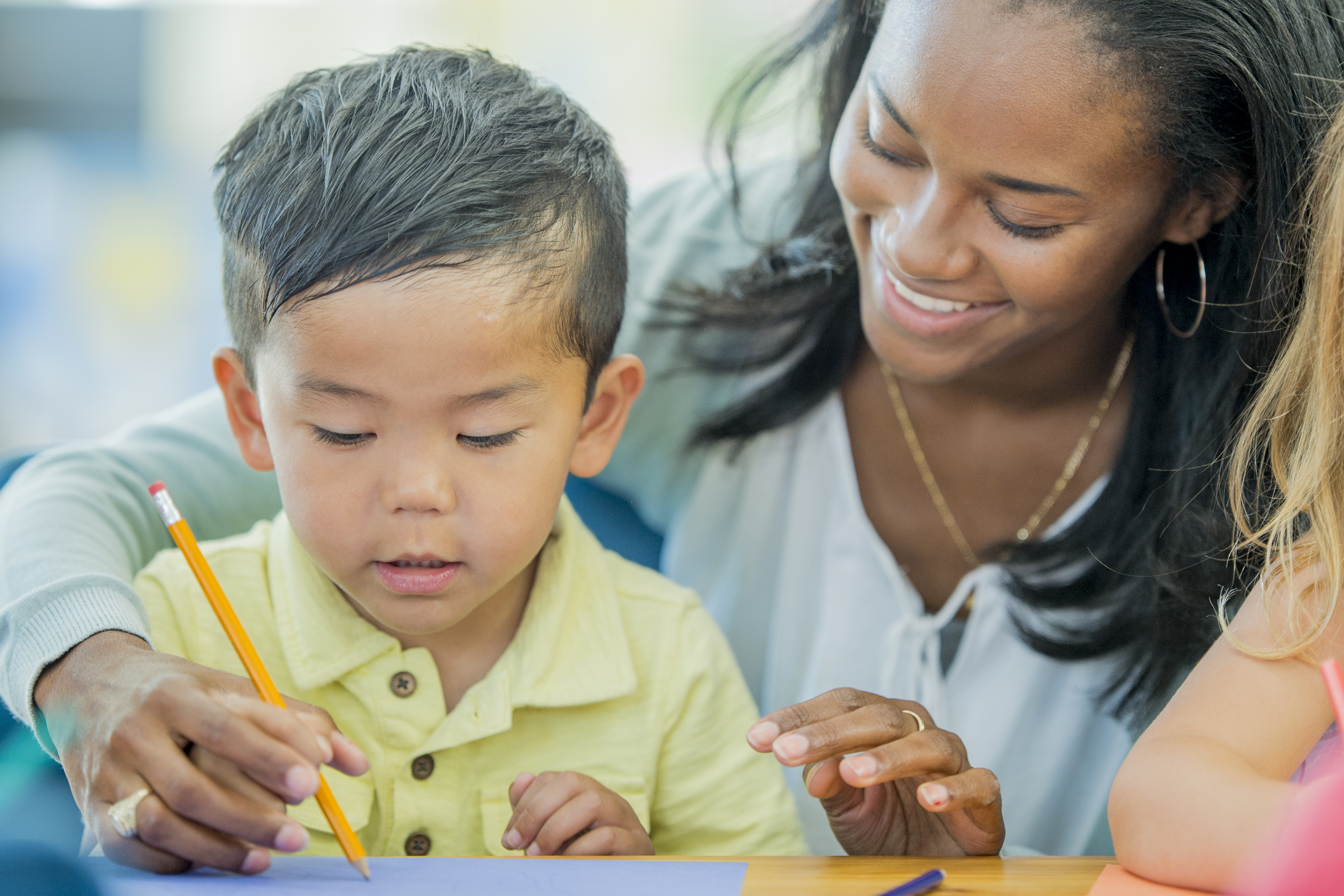 A teacher is helping a preschool students learn how to use his pencil.