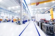 Horizontal image of huge new modern factory with robots and machines producing industrial plastic pieces and equipment. Wide angle view of futuristic machines and long aisle.