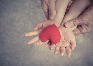 old hands holding young hands of a baby with red heart / Love and relationship in a family