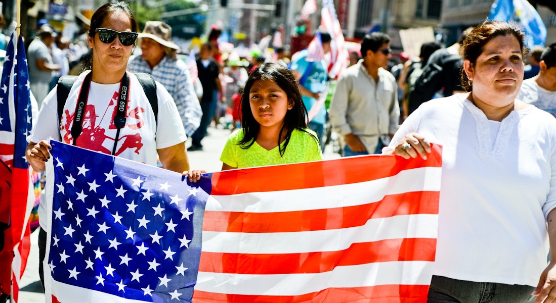 Los Angeles, USA - May 1, 2013: May Day March in Los Angeles Downtown, USA. People holding banners representing different social structures, organizations. March was mostly dedicated to Immigration reform discussed. Two women and teenager girl are holding big American flag.