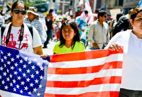 Los Angeles, USA - May 1, 2013: May Day March in Los Angeles Downtown, USA. People holding banners representing different social structures, organizations. March was mostly dedicated to Immigration reform discussed. Two women and teenager girl are holding big American flag.