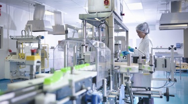 Worker inspecting products on production line in pharmaceutical factory