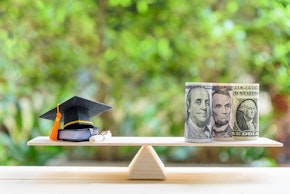 Money cost saving for goal and success in school, education concept : US USD dollar notes or cash, graduation cap, a text book, a certificate / diploma on basic wooden balance scale. Green background.