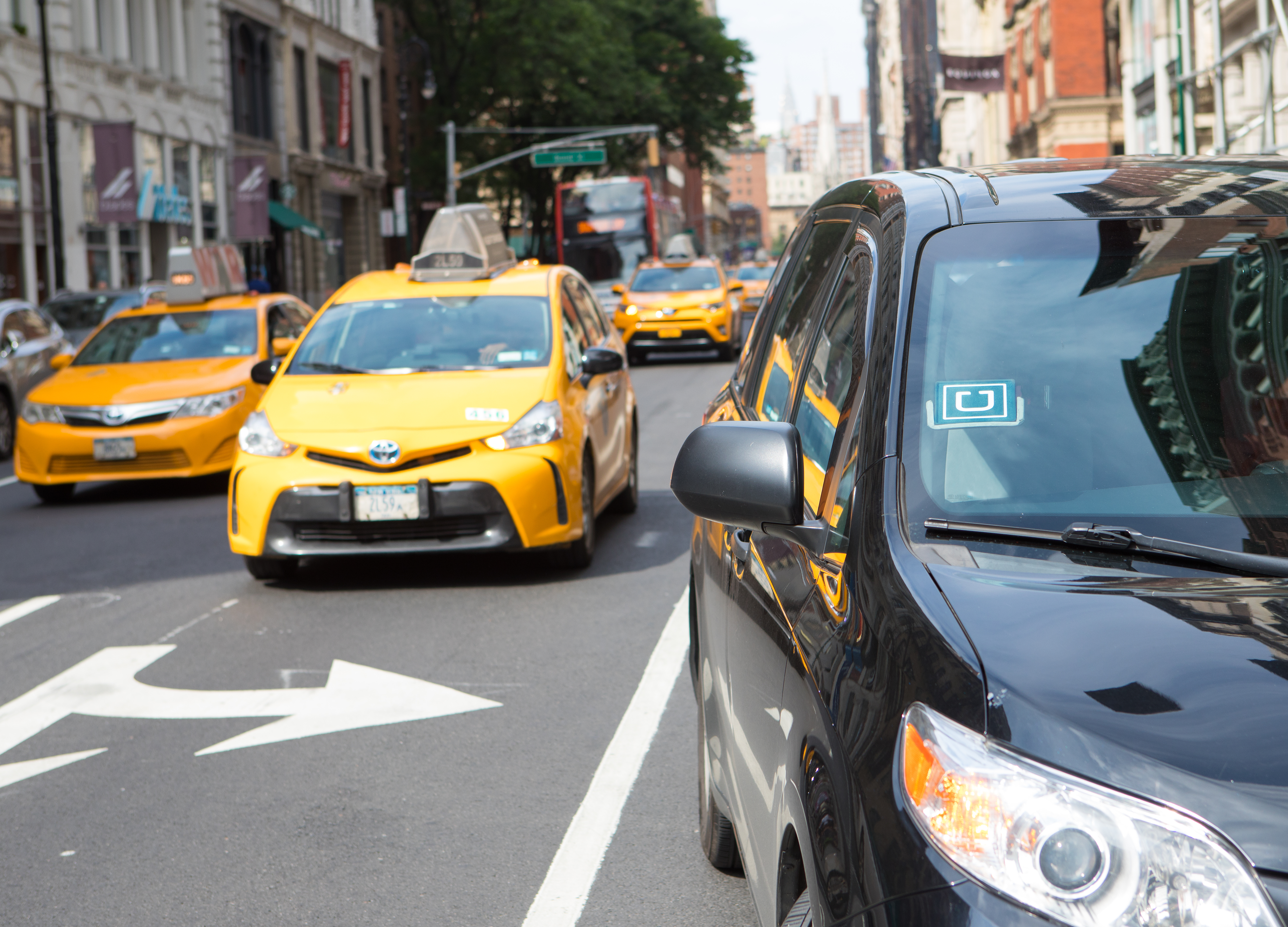 New York, USA - July 8, 2017: Uber car service in foreground picking up passenger on Broadway in Lower Manhattan shopping district.  Customer call on an Uber car by using an app on the mobile phone