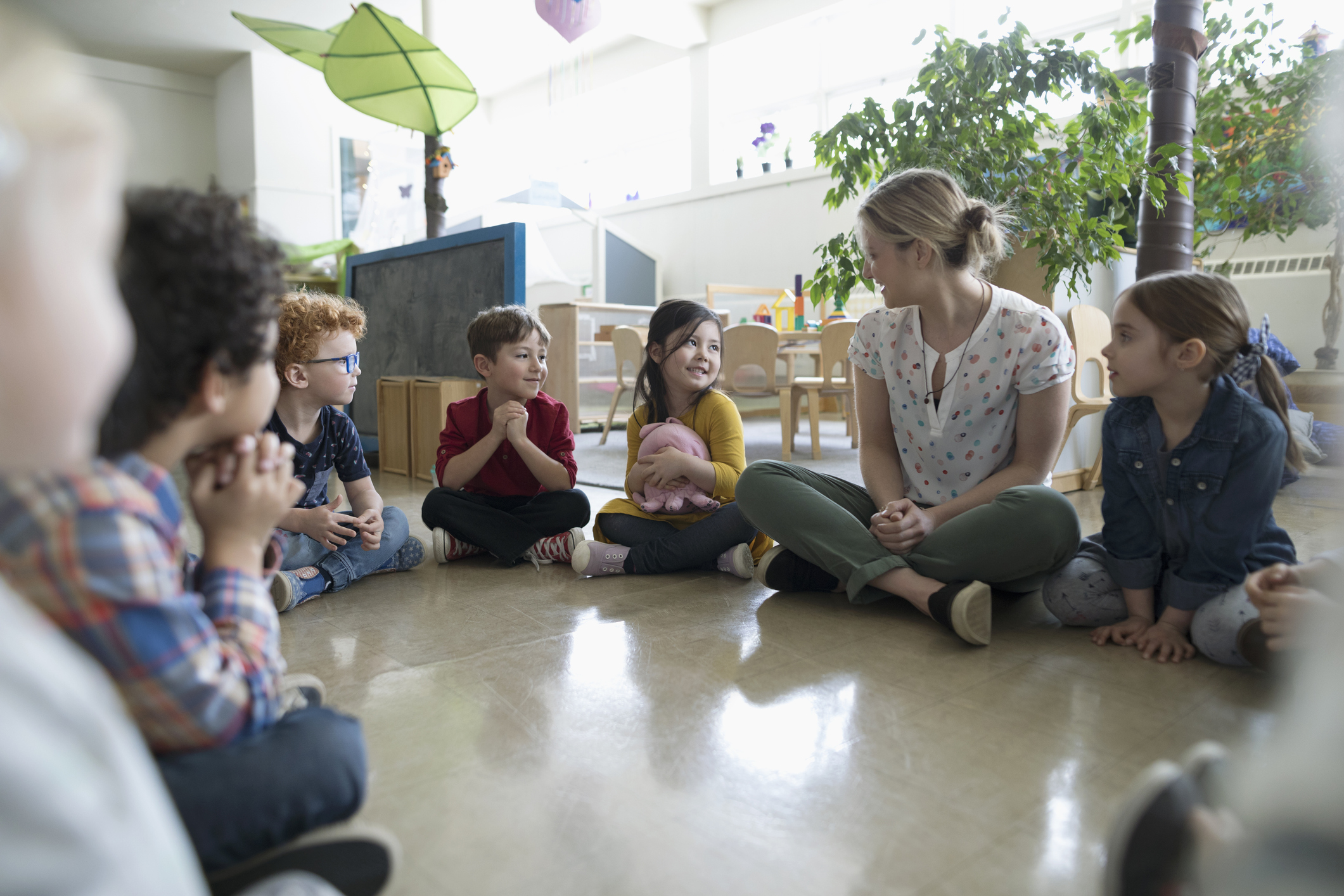 a group of children sitting on the floor talking to a woman