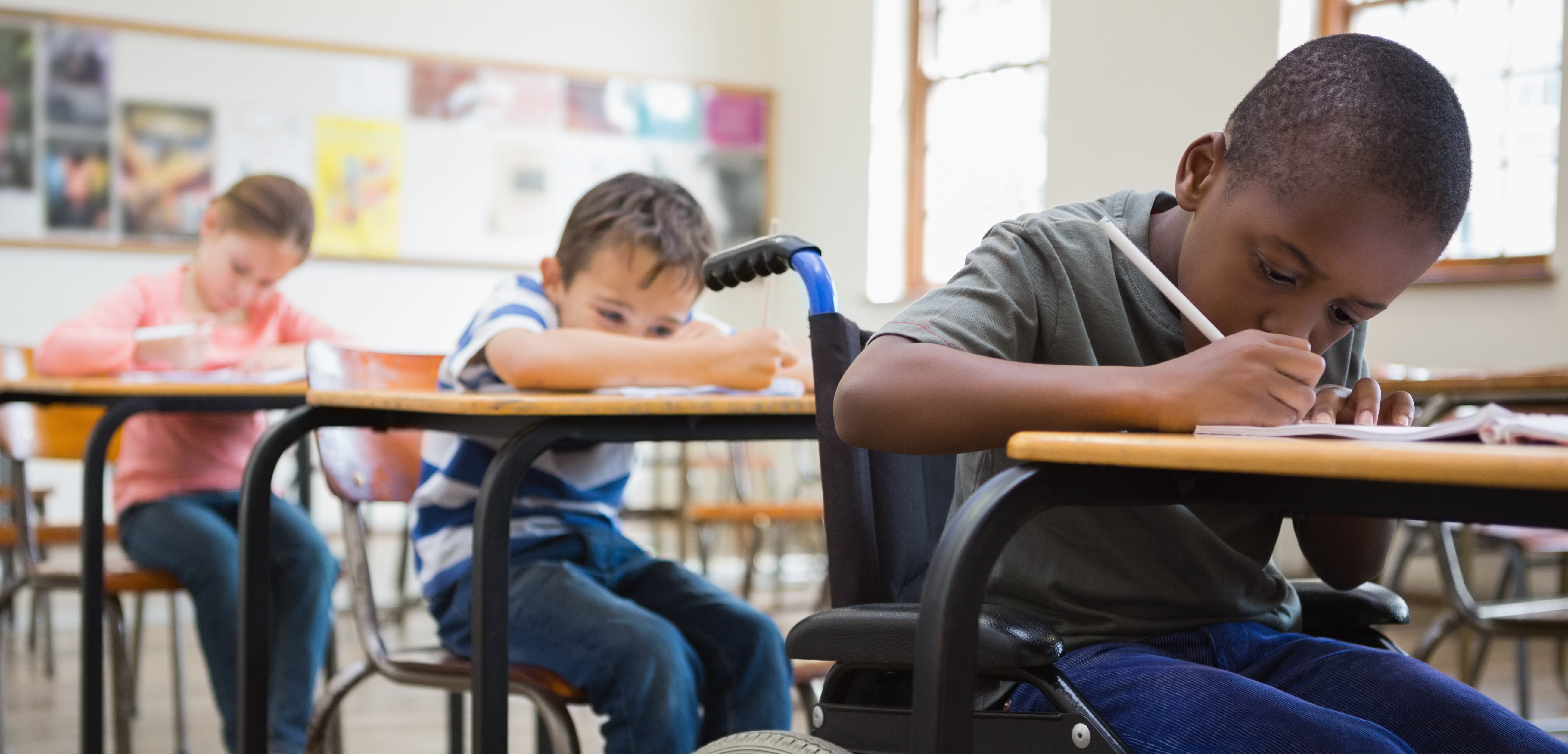Cute pupils writing at desks in classroom at the elementary school