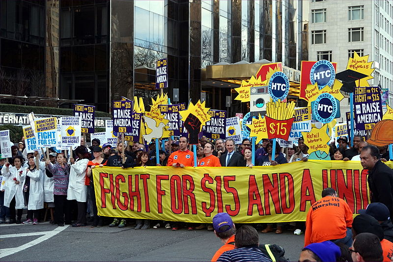 A photograph of a demonstration in a city advocating for the fight to raise the minimum wage.