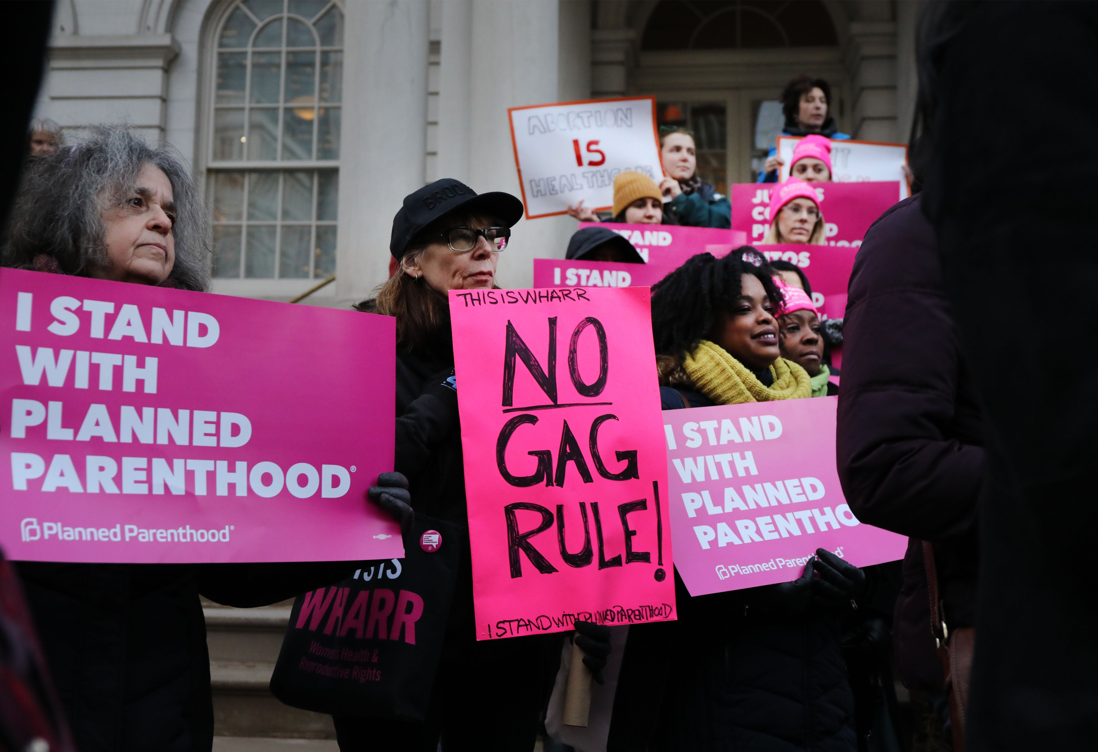 a group of people holding pink signs in front of a building