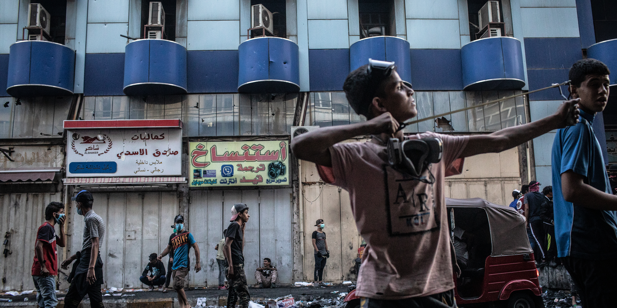 A young Iraqi protestor launches rocks at Iraqi security forces with his slingshot near Al-Senak Bridge in Baghdad