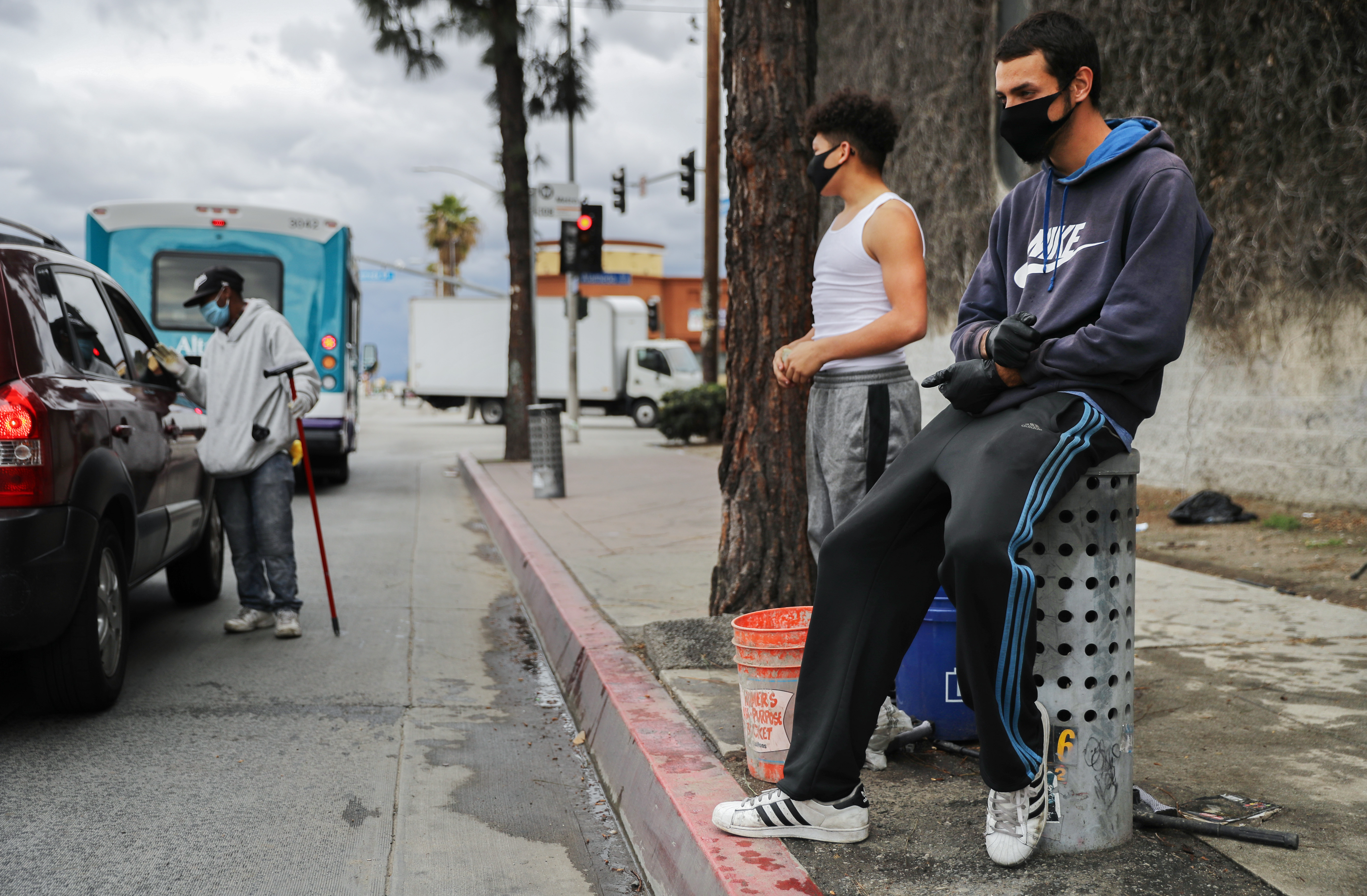 LOS ANGELES, CALIFORNIA  - APRIL 06: Young men wear face masks while waiting to clean windshields for extra cash amid the coronavirus pandemic on April 6, 2020 in south Los Angeles, California. More than 10,000 people have now died in the U.S. from COVID-19. (Photo by Mario Tama/Getty Images)