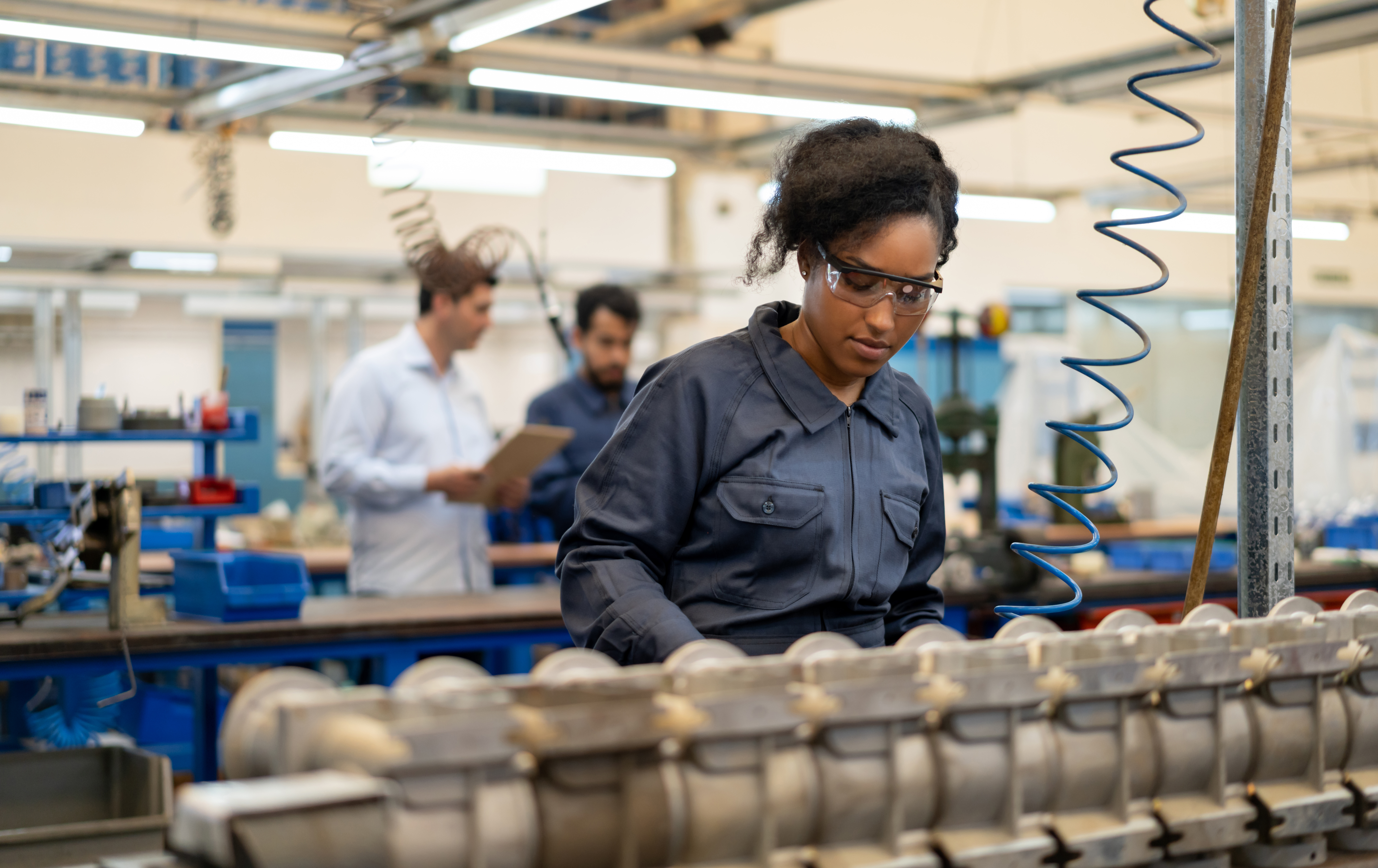 African american young woman working at an assembly production of water pumps at a factory - Incidental people at background