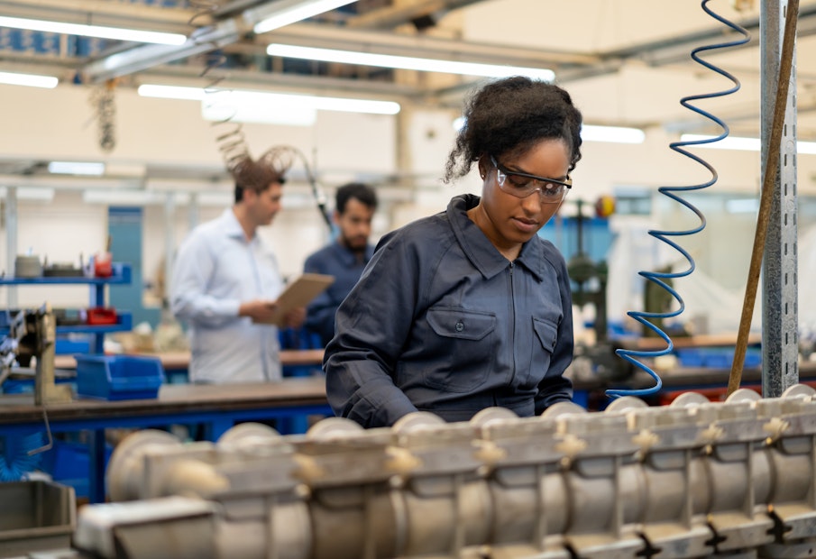 African american young woman working at an assembly production of water pumps at a factory - Incidental people at background