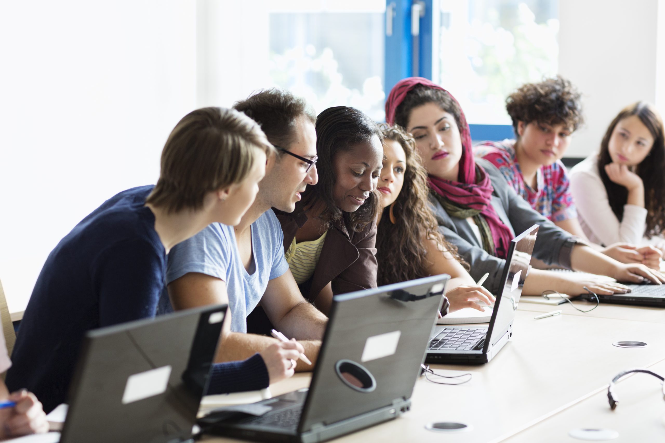 teacher explaining something to group of students in classroom with pc, sitting in a row,, focus on teacher