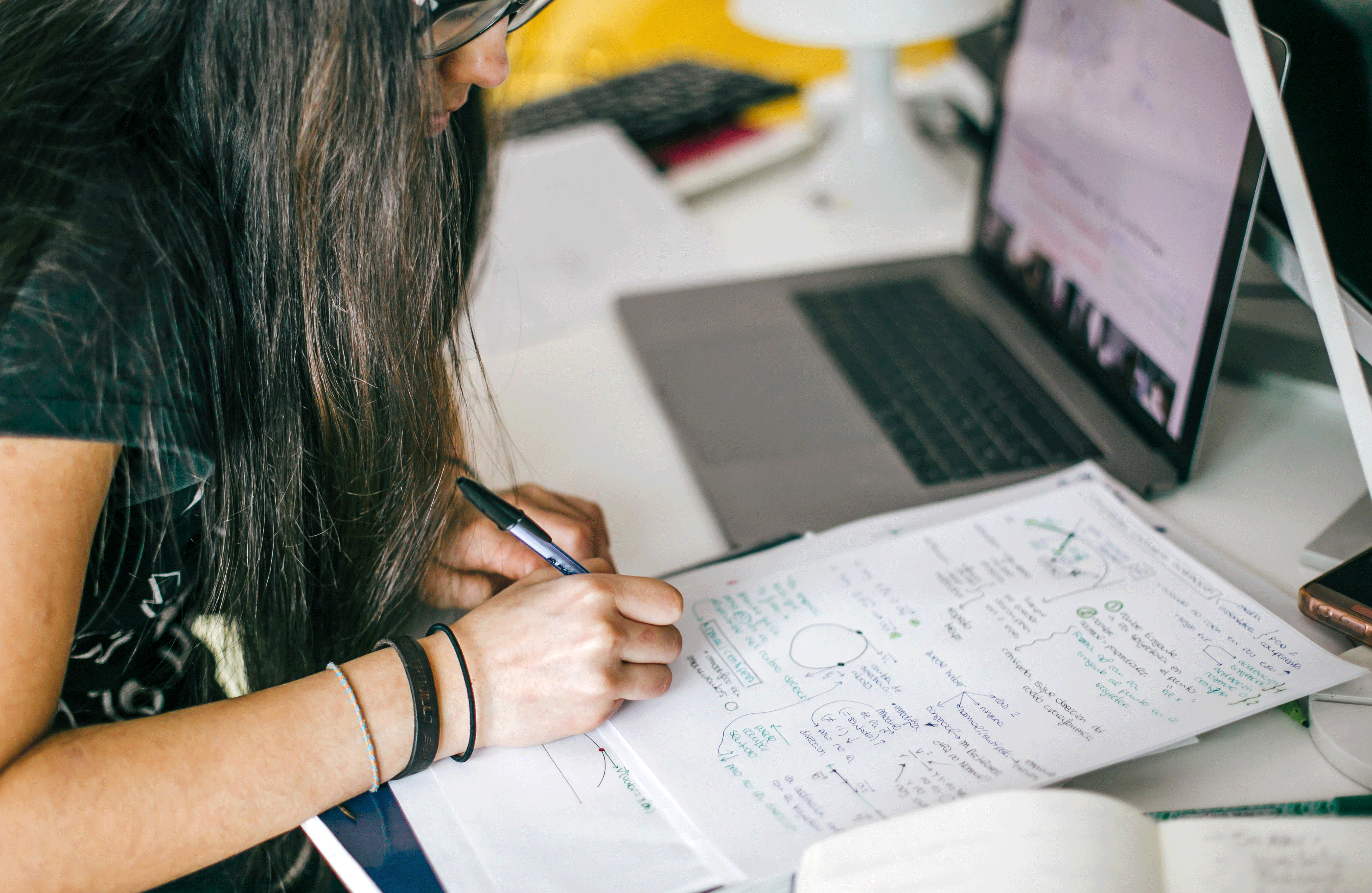 a woman writing on a piece of paper next to a laptop