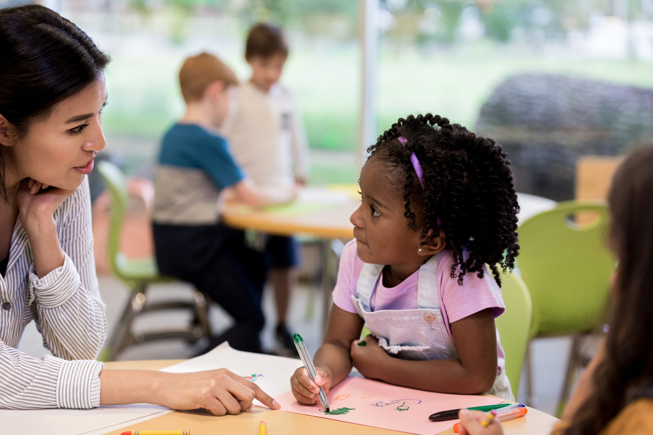 Caring female art teacher helps a young girl with her drawing during art class.