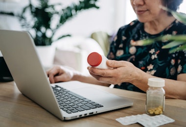 Senior Asian woman video conferencing with laptop to connect with her family doctor, consulting about medicine during self isolation at home in Covid-19 health crisis