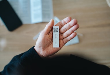 Overhead view of senior Asian woman carrying out a Covid-19 rapid lateral flow test at home. She is holding a positive Coronavirus rapid self test device, feeling worried