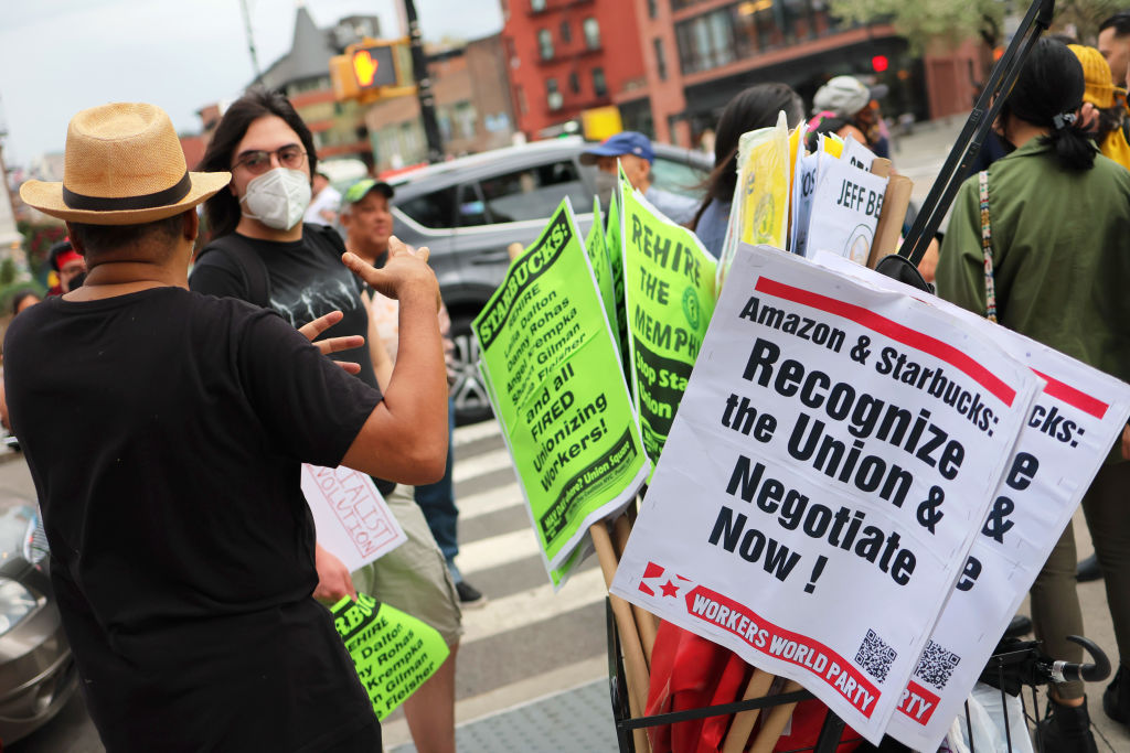NEW YORK, NEW YORK - APRIL 14: People hold signs while protesting in front of Starbucks on April 14, 2022 in New York City. Activists gathered to protest Starbucks' CEO Howard Schultz anti-unionization efforts and demand the reinstatement of workers fired for trying to unionize. (Photo by Michael M. Santiago/Getty Images)