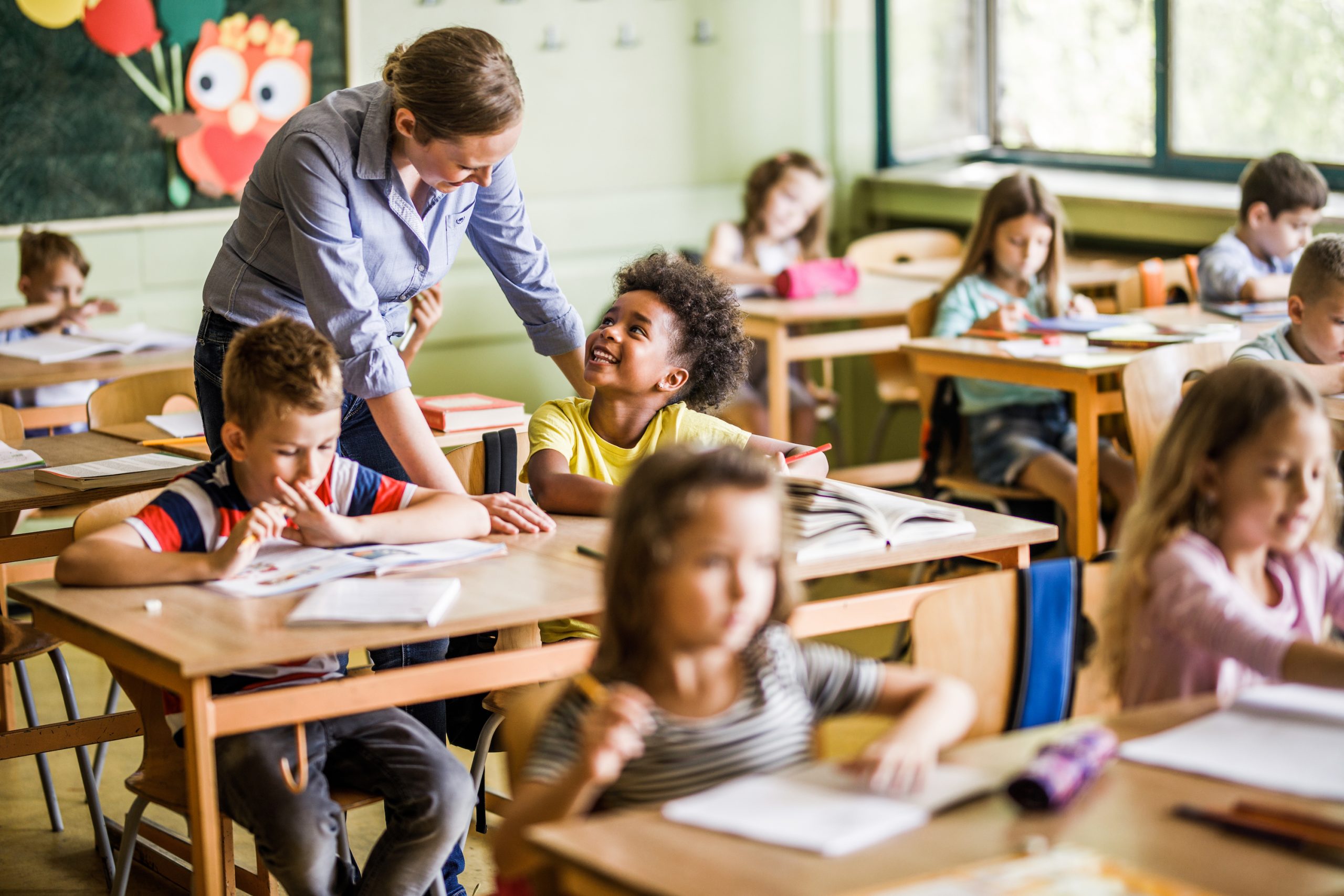 Happy African American elementary student communicating with her female teacher who is assisting her in the classroom.
