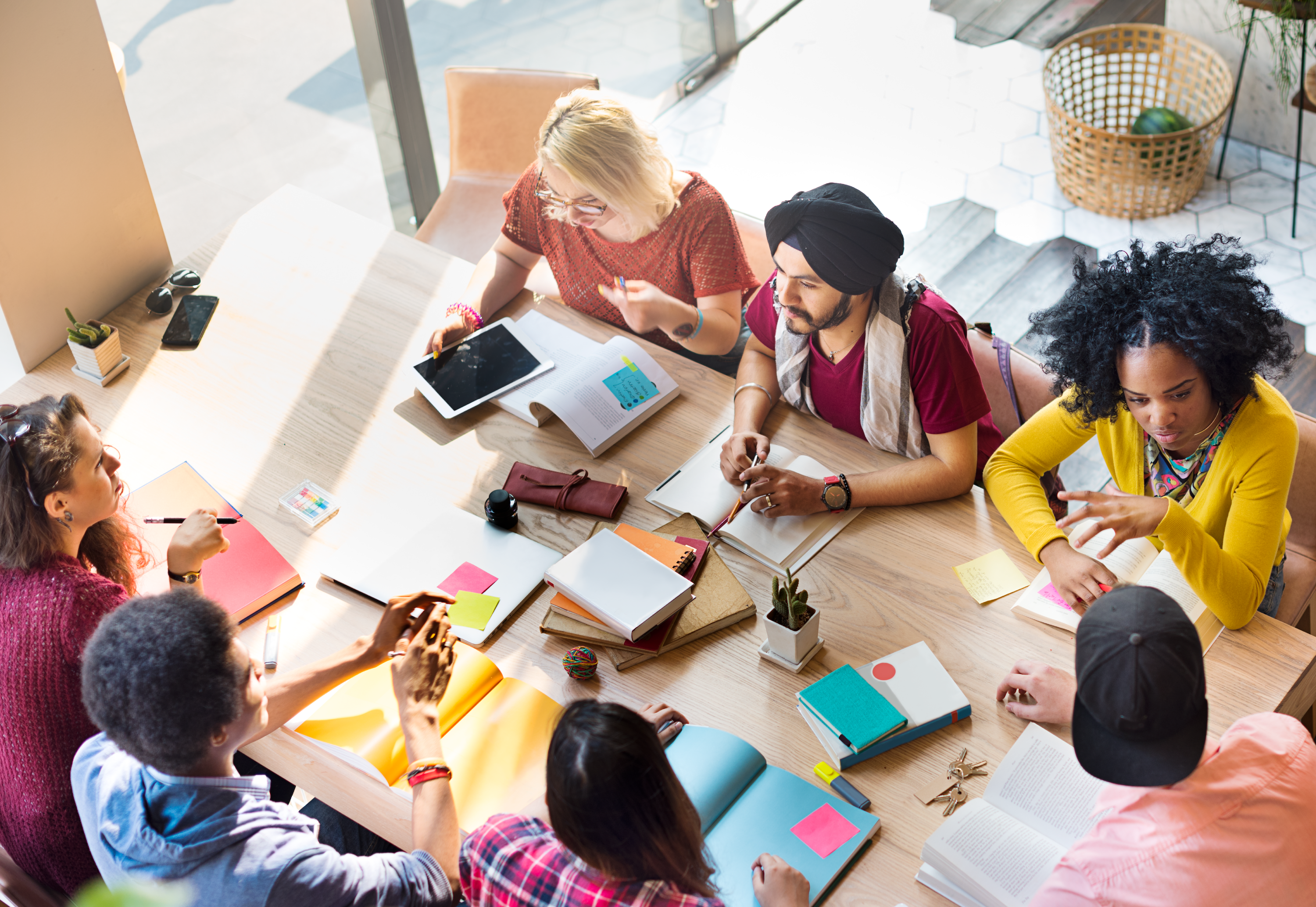 A group of students are sitting together at a wooden table talking and collaborating.