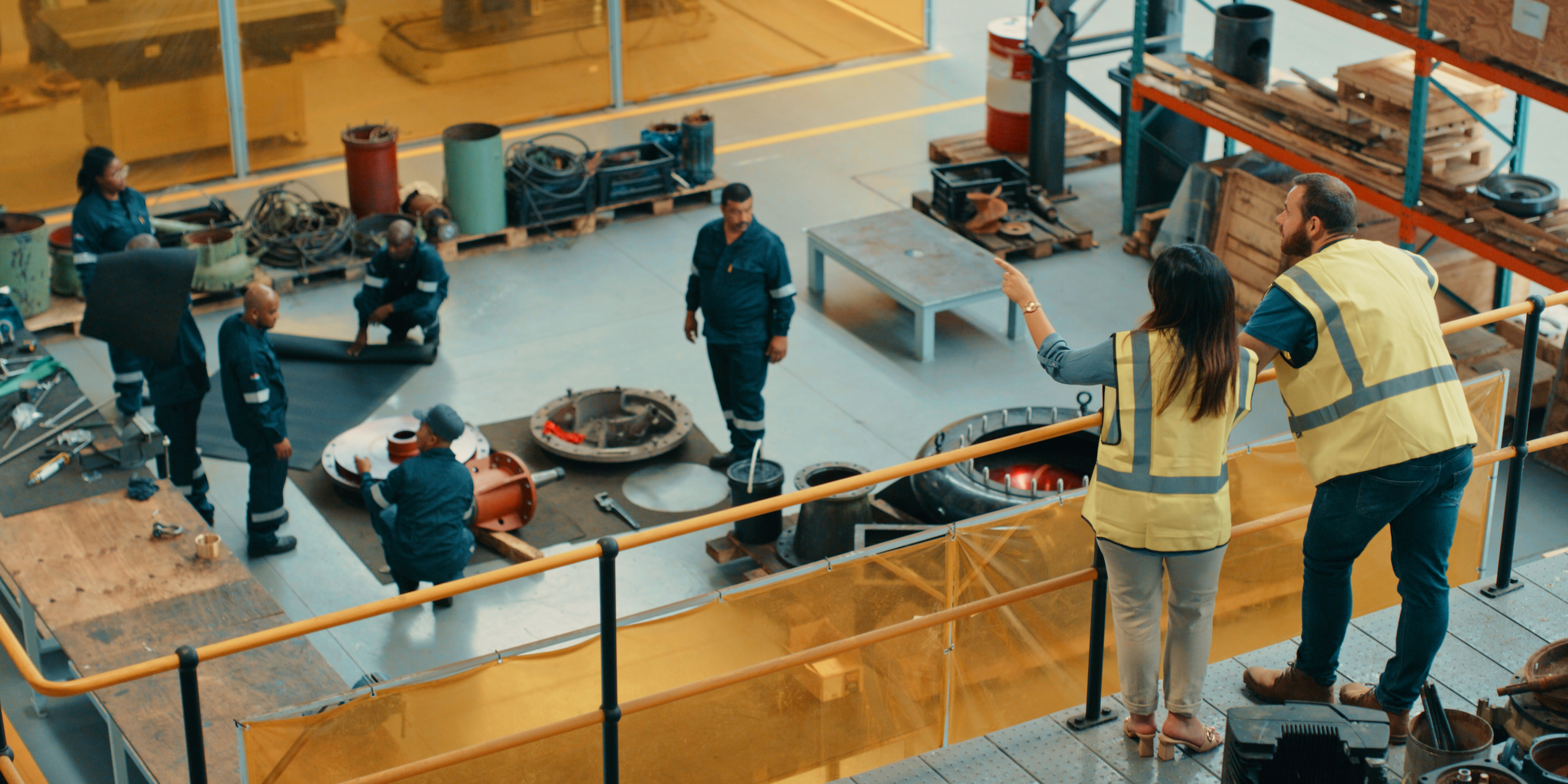 Two managers at a manufacturing warehouse watching over workers in the factory.