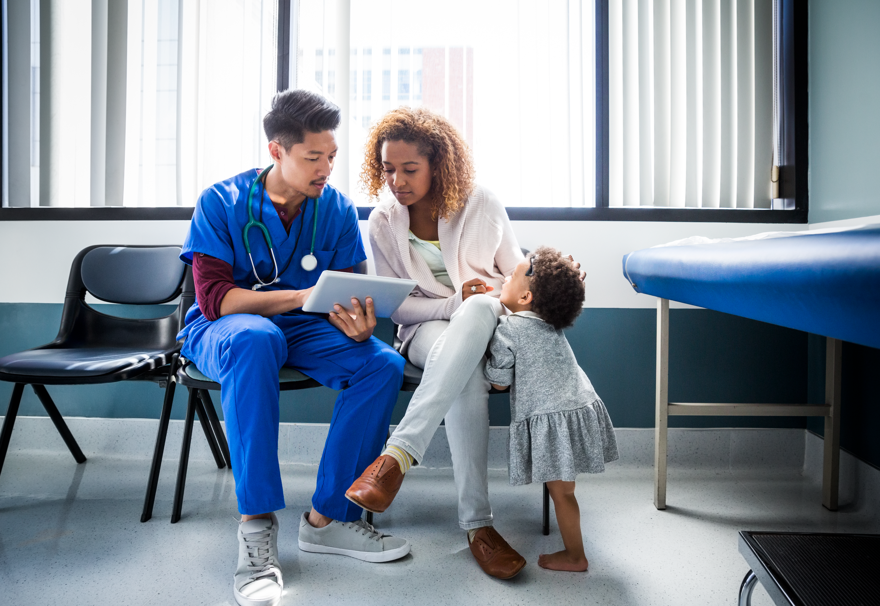 A nurse showing digital tablet to mother and child in a hospital.