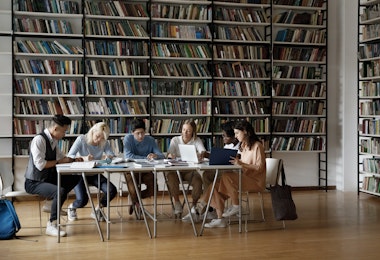 A group of students sitting at a table surrounded by bookcases.
