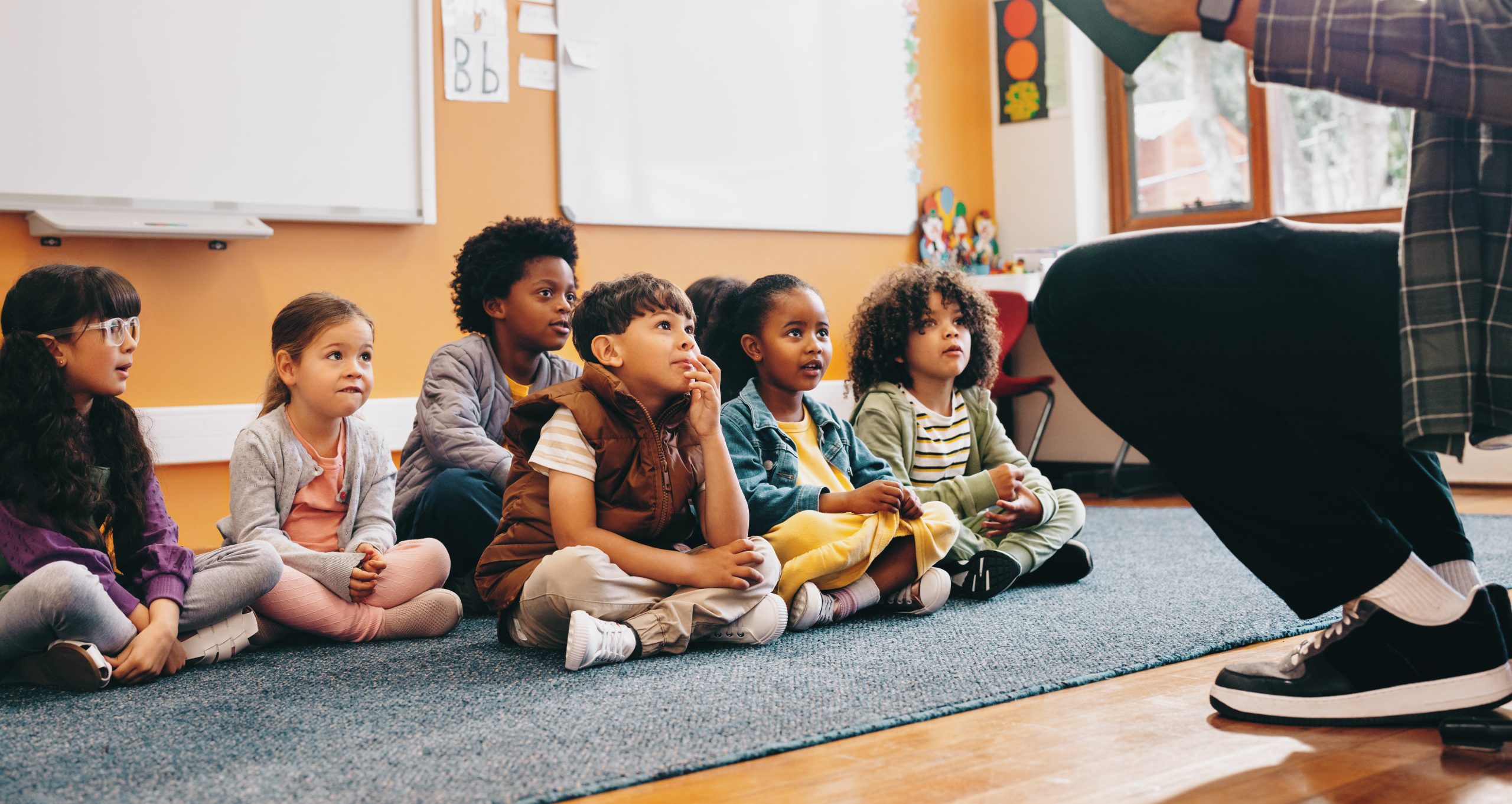 Elementary school students sit and listen to a story from their teacher. Group of young children having a listening comprehension lesson in class. Kids schooling in a multiethnic education centre.