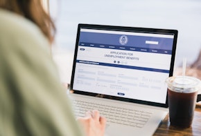 An over the shoulder photo of an unrecognizable woman applying for unemployment benefits. She is using the government website.