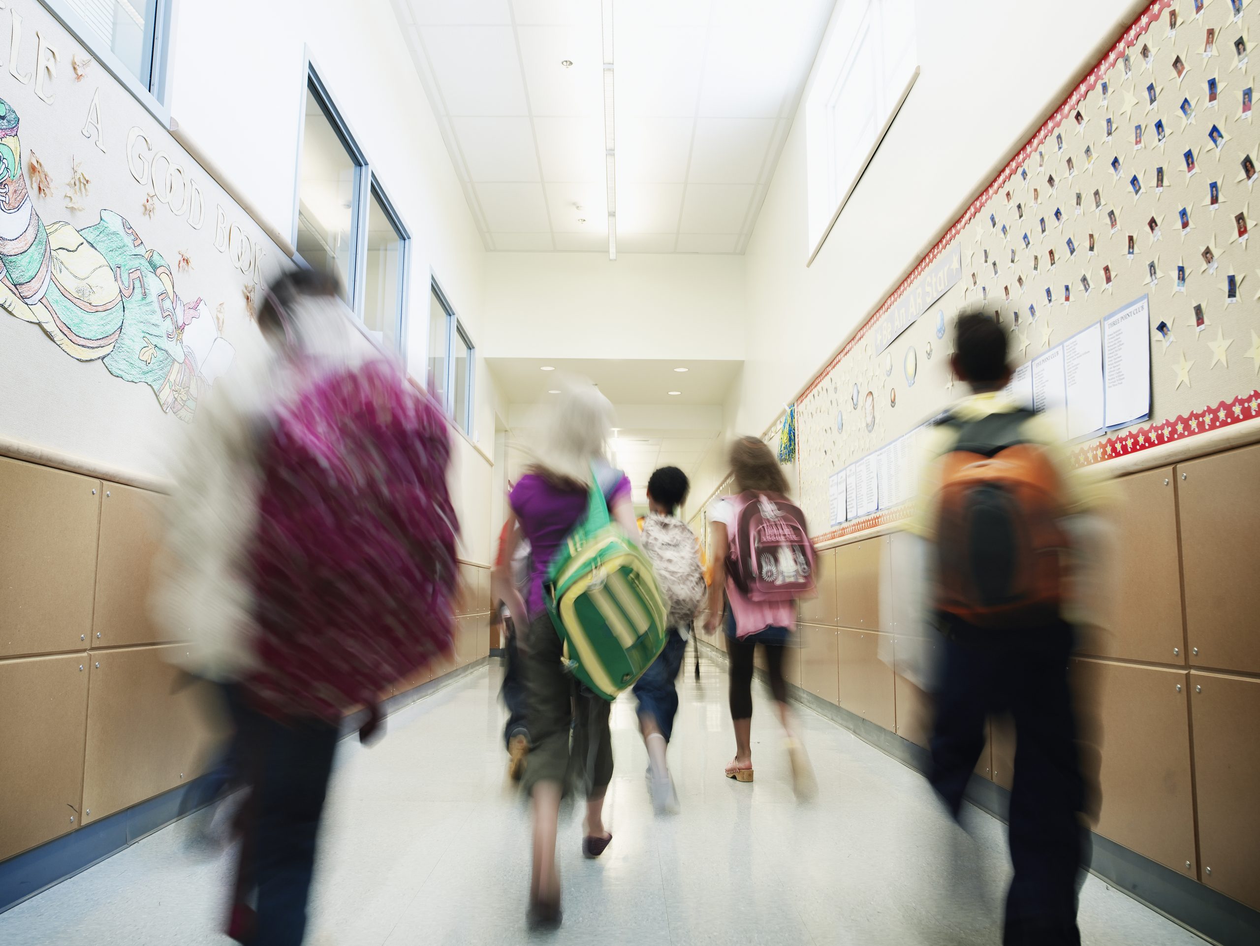 Young students with backpacks walking down hallway of elementary school