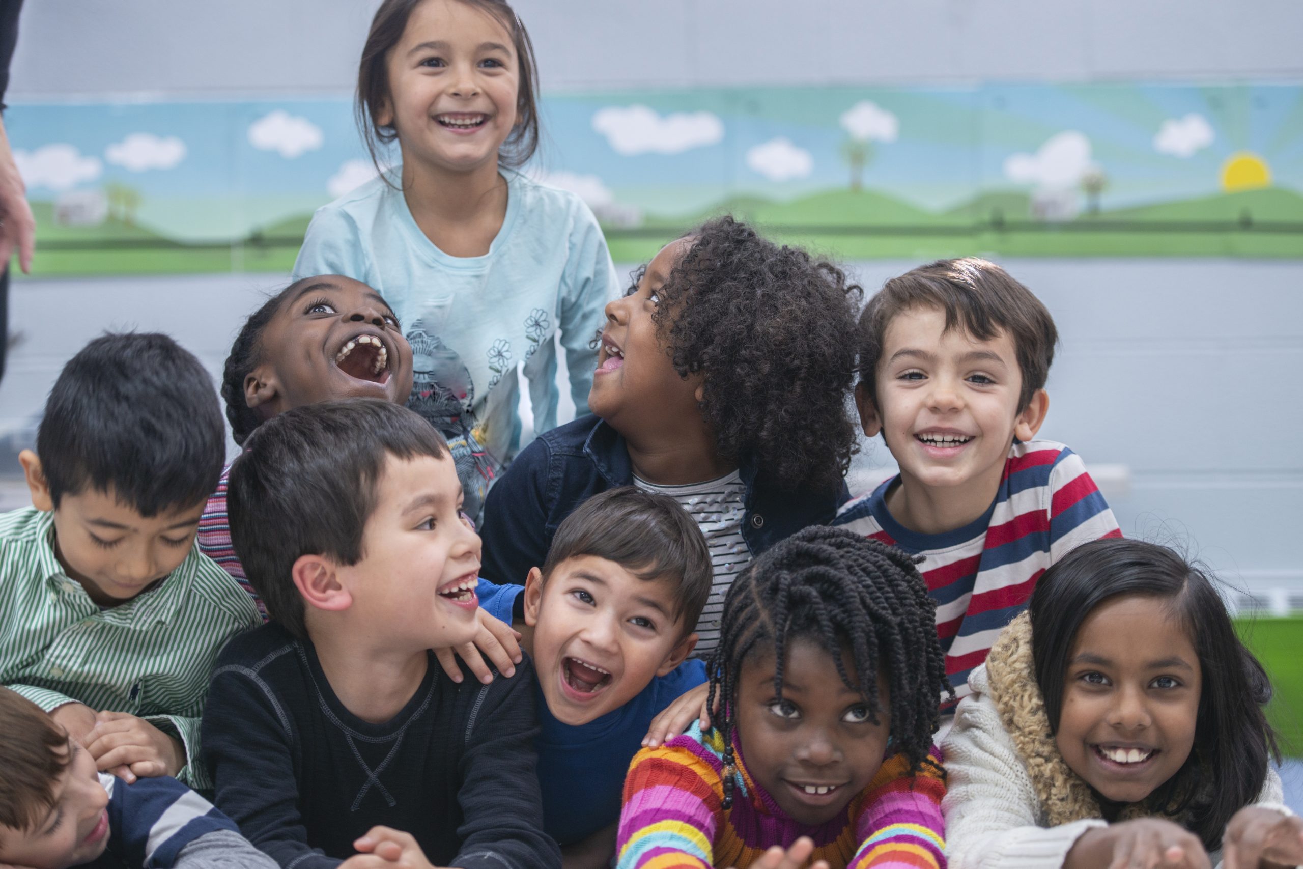 A cute little boy smiles at his friend as he tries to stay focused to finish an in-class assignment. He is slightly unfocused as something across the room grabs his attention.