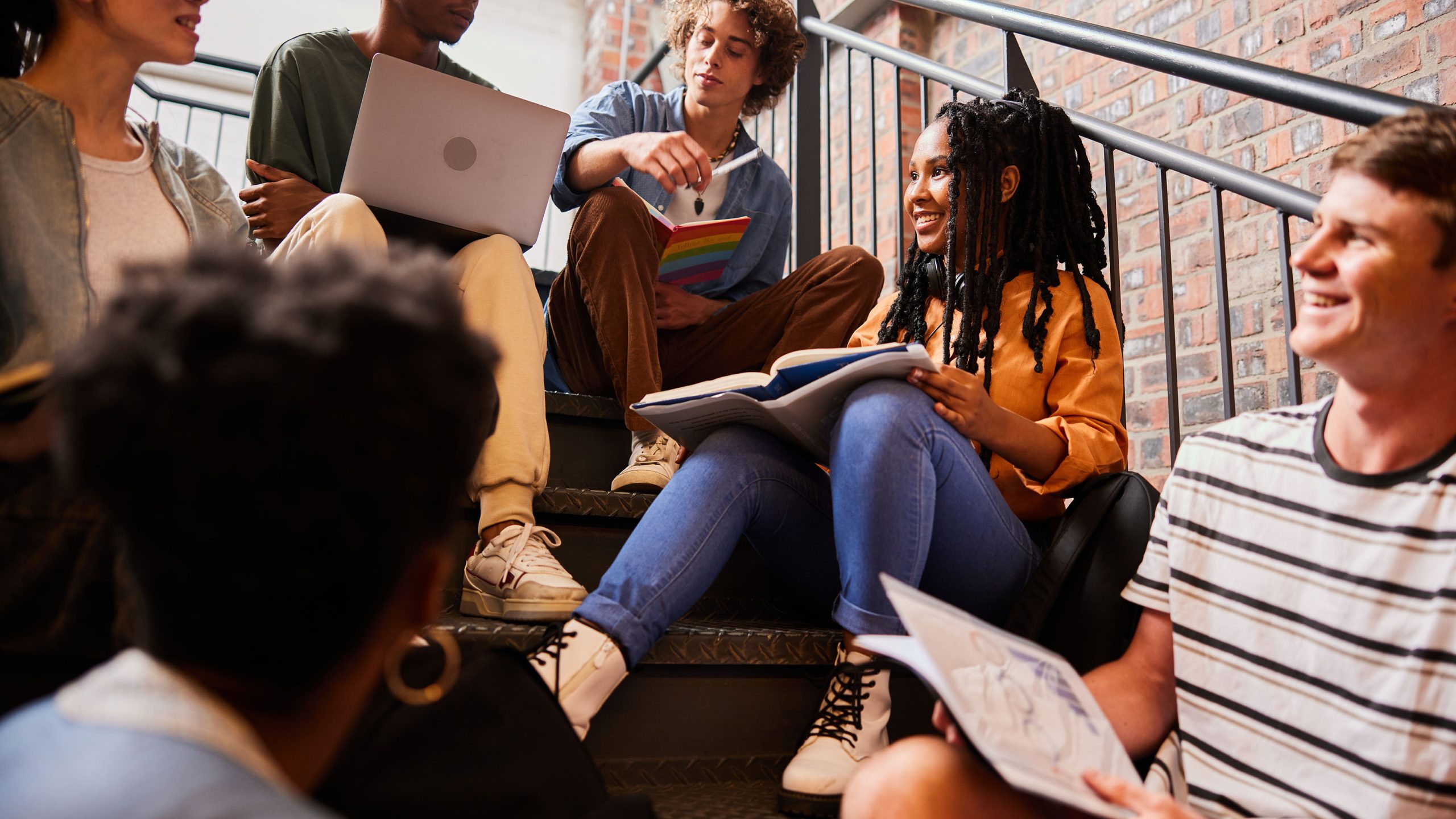 Diverse group of smiling young college students talking while studying together on stairs at school between classes