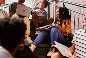 Diverse group of smiling young college students talking while studying together on stairs at school between classes