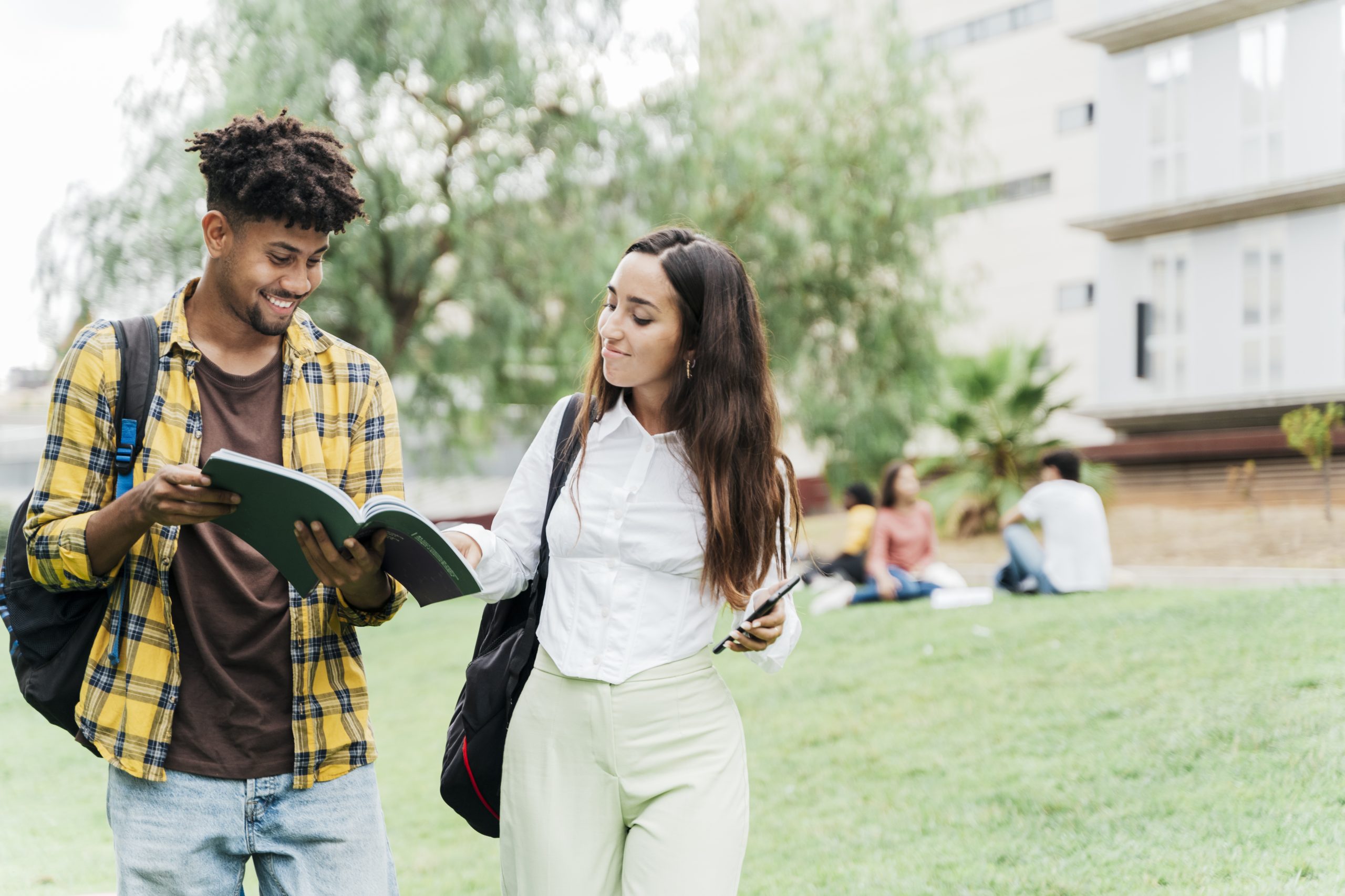 Multiracial couple of university students outside the university looking at a book (Concept of university studies).