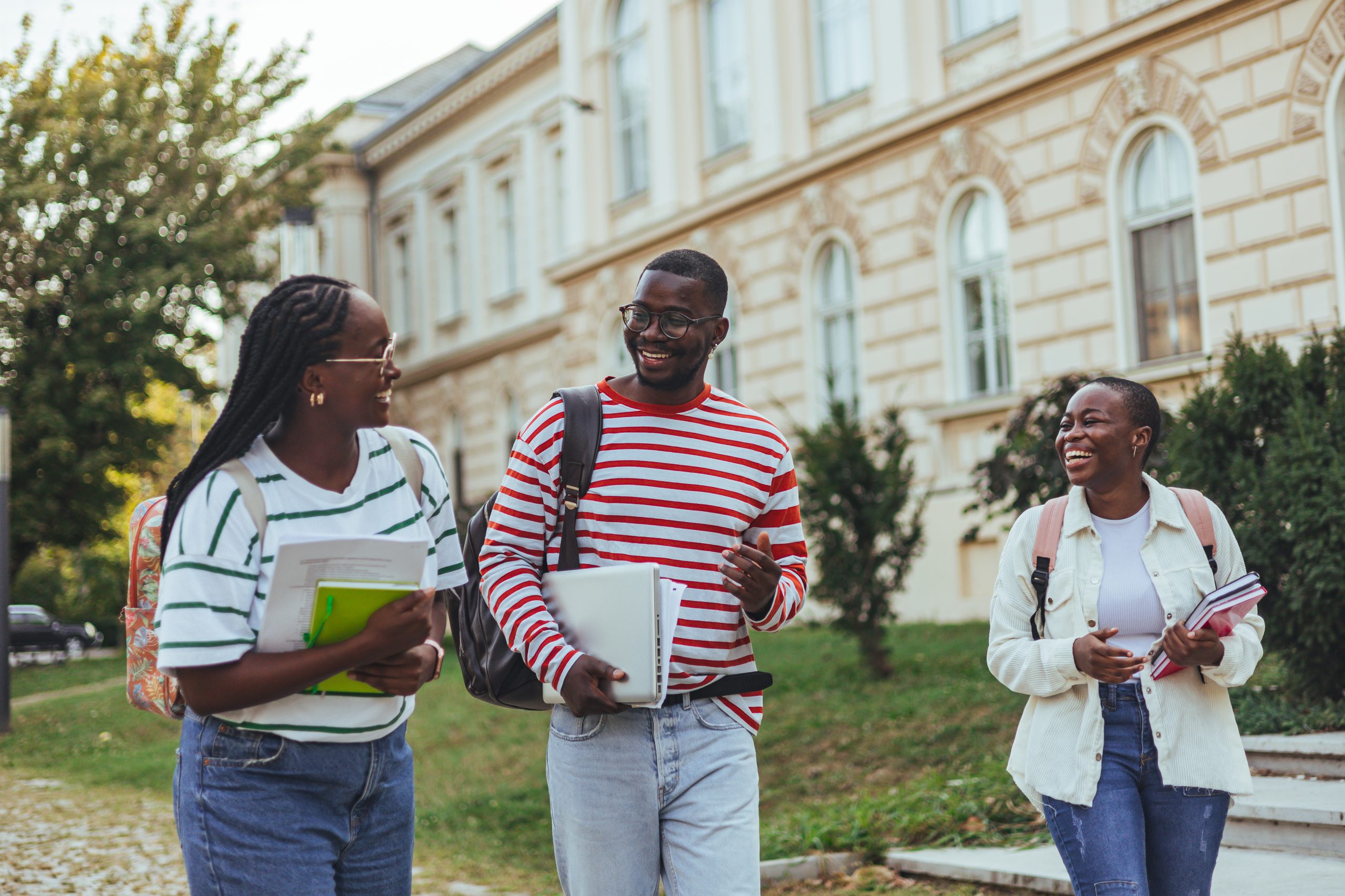 Group of happy young friends sitting in college campus and talking. Cheerful group of smiling girls and guys feeling relaxed after university exam. Excited millenials laughing and having fun outdoor.