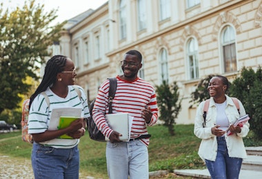 Group of happy young friends sitting in college campus and talking. Cheerful group of smiling girls and guys feeling relaxed after university exam. Excited millenials laughing and having fun outdoor.