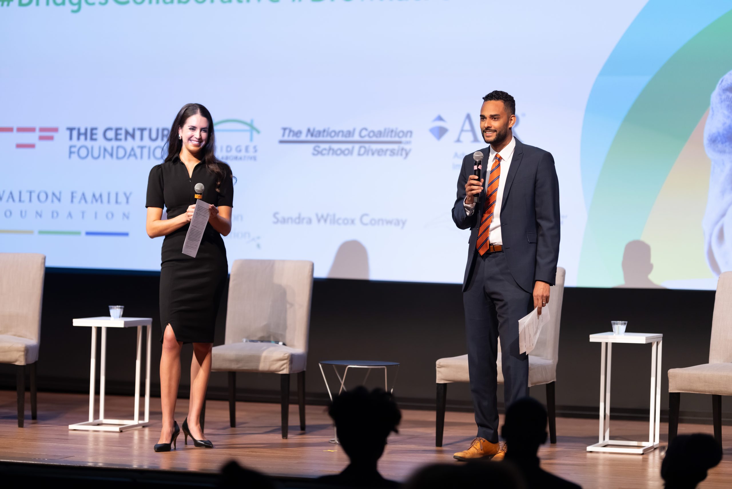 Dr. Stefan Lallinger holds a microphone on stage in front of a large projection screen.