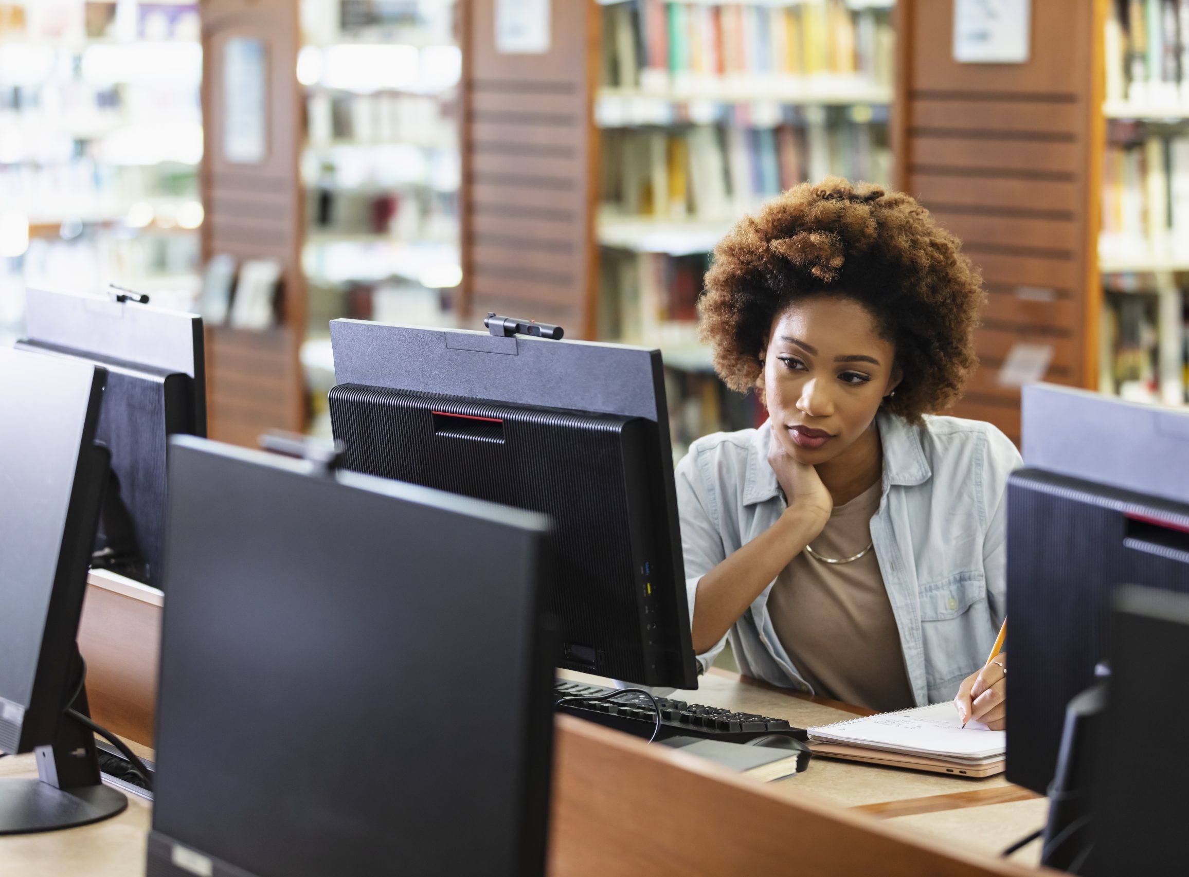 A young African-American woman in her 20s using a desktop computer in the library.
