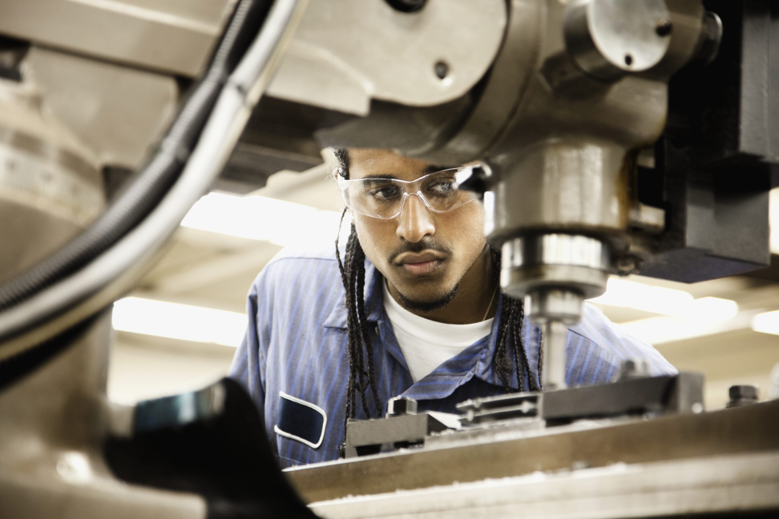 Young hispanic man using machine in machine shop