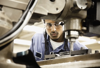 Young hispanic man using machine in machine shop